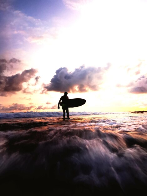 Foto hombre silueta de pie en el mar contra el cielo durante la puesta de sol