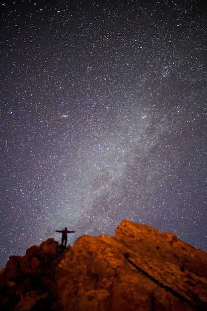 Foto hombre silueta de pie en la montaña contra el campo de estrellas por la noche