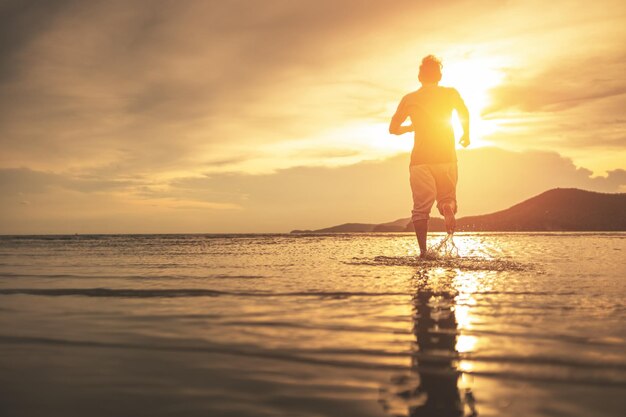 Hombre silueta de pie en la playa durante la puesta de sol