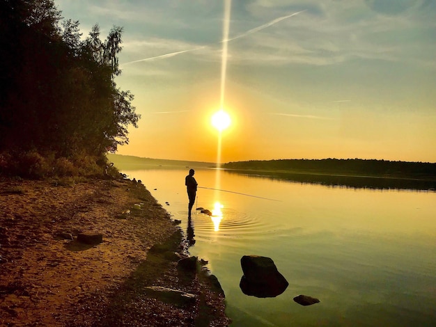 Foto hombre silueta de pie en la roca contra el cielo durante la puesta de sol