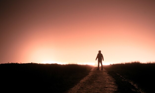 Foto hombre silueta de pie en tierra contra el cielo durante la puesta de sol