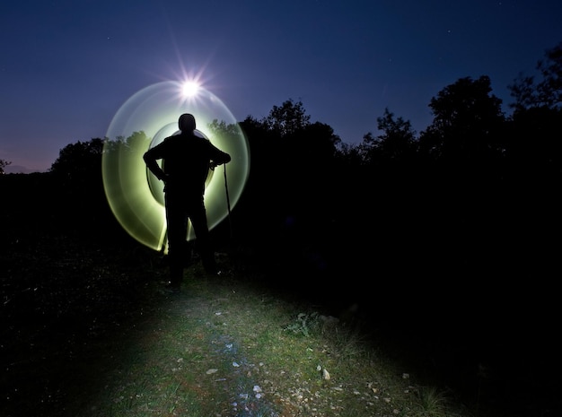 Foto hombre silueta con pintura de luz de pie en tierra contra el cielo despejado