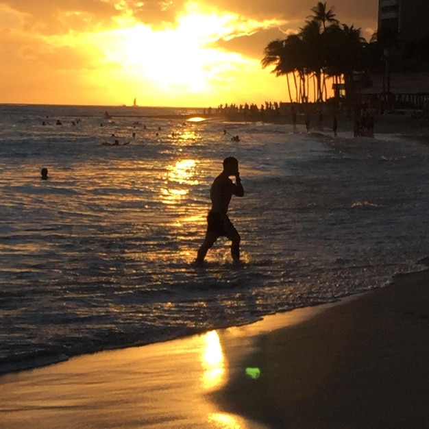 Hombre silueta en la playa contra el cielo durante la puesta de sol