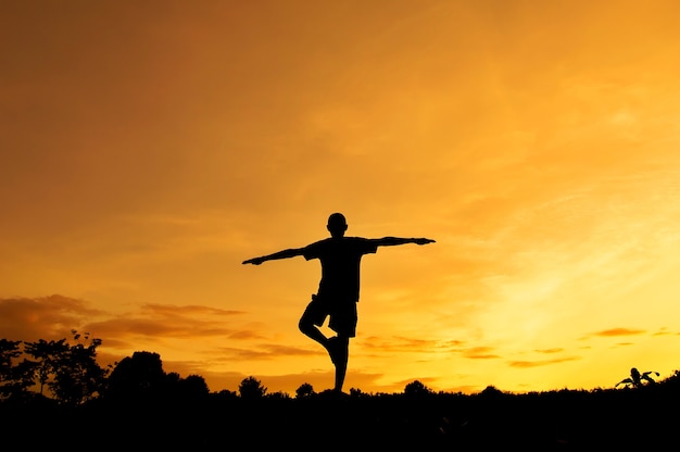 Hombre de silueta practicando yoga con cielo al atardecer