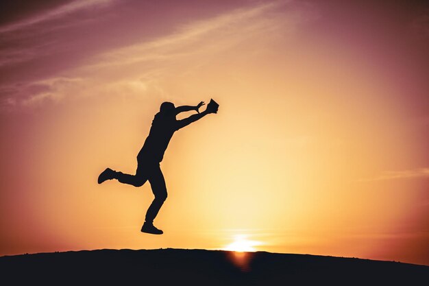 Foto hombre silueta saltando contra el cielo durante la puesta del sol