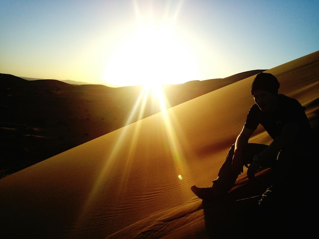Hombre silueta sentado en una duna de arena contra el cielo en el desierto del Sáhara durante un día soleado