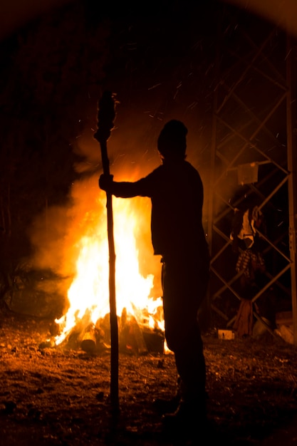 Hombre silueta sosteniendo bambú mientras mira el fuego durante la noche