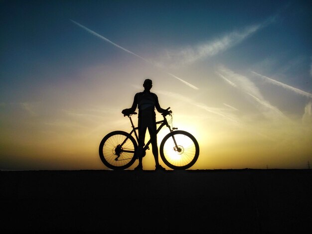 Hombre silueta sosteniendo una bicicleta en el campo durante la puesta de sol