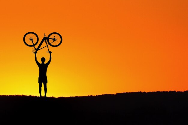 Hombre silueta sosteniendo una bicicleta mientras está de pie en el campo contra el cielo durante la puesta de sol