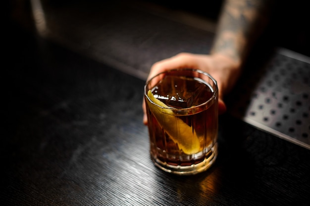 Hombre sirviendo una copa de un cóctel Rusty Nail con ralladura de naranja en la barra del bar