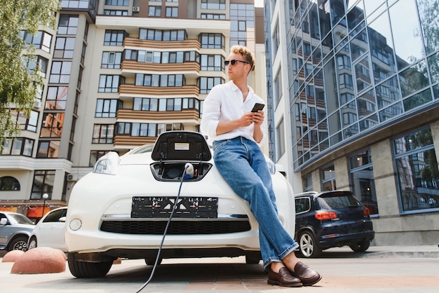 Hombre con smartphone después de terminar de cargar la batería. Hombre cerca de vehículo eléctrico