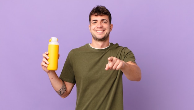 Hombre con smoothy apuntando a la cámara con una sonrisa satisfecha, confiada y amistosa, eligiéndote