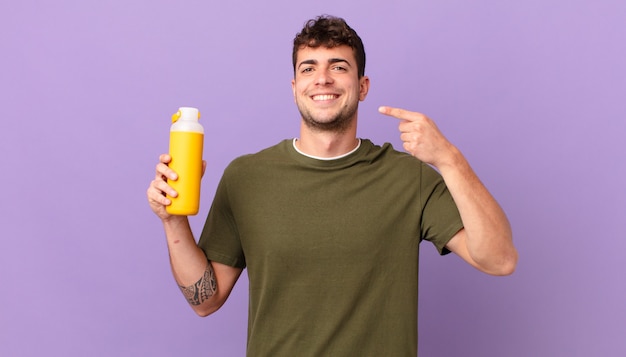 Hombre con smoothy sonriendo con confianza apuntando a su propia sonrisa amplia, actitud positiva, relajada y satisfecha