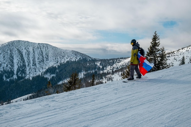 Hombre snowboarder con bandera de eslovaquia en la pendiente de la estación de esquí