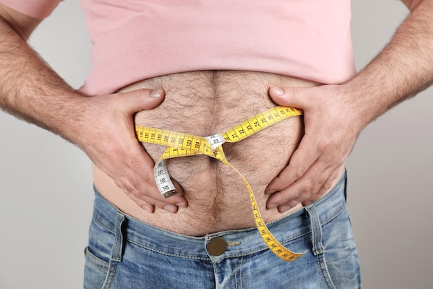 Hombre con sobrepeso con barriga grande y cinta métrica en primer plano de fondo de color