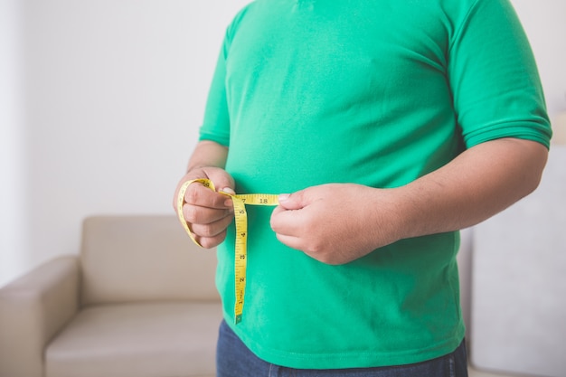 Hombre con sobrepeso midiendo su vientre en casa