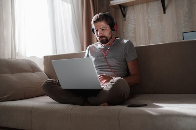 Hombre en el sofá con auriculares y portátil en casa