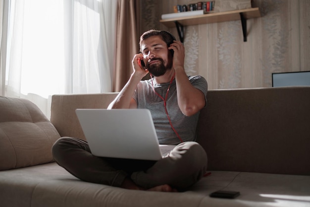 Hombre en el sofá con auriculares y portátil en casa