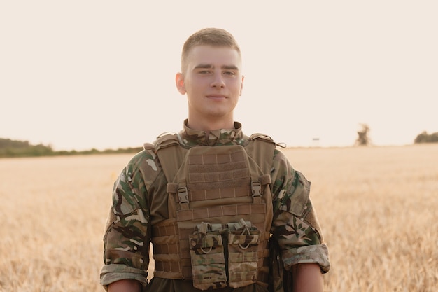 Hombre soldado de pie contra un campo. Retrato de feliz soldado militar en el campo de entrenamiento.