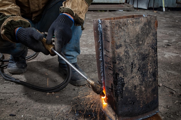 Hombre soldador en uniforme de construcción de máscara de soldadura y guantes protectores negros elabora una máquina de soldadura de metal en la fábrica en el sitio de construcción de fondo