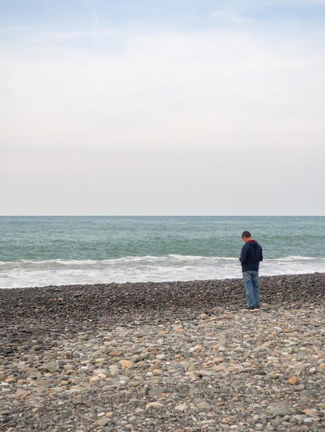 Foto hombre solitario en la orilla del mar mira las olas camina a lo largo de la costa fuera de temporada en el balneario otoño en el sur subtropicales en el frío