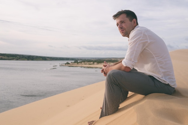 Hombre solitario sentado en la playa de arena y mirando vistas de lejos solo