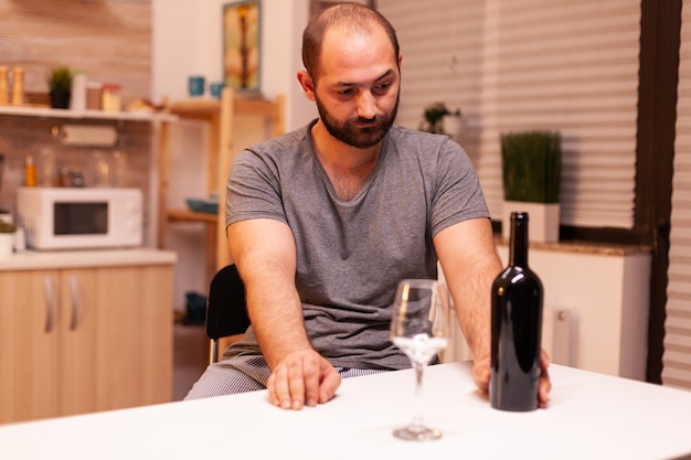 Hombre solitario sosteniendo una botella de vino tinto debido a la depresión. Enfermedad de la persona infeliz y ansiedad sensación de agotamiento con síntomas de mareos que tienen problemas de alcoholismo.