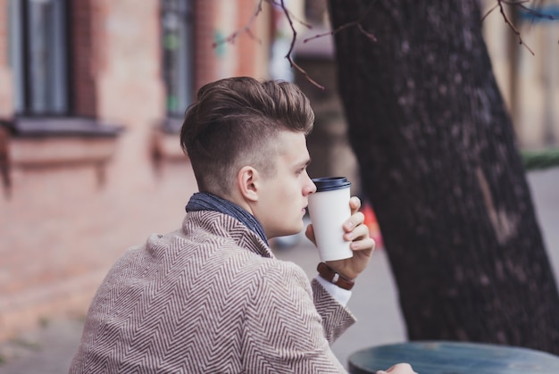 Hombre solitario sostiene un café para llevar mientras está sentado en un café de la calle