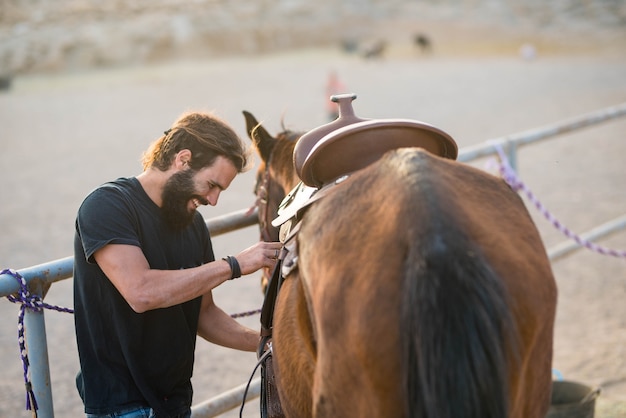 Foto un hombre solo en un rancho cuidando un caballo - sonriendo y divirtiéndose arreglando - caballo listo para correr y listo para irse con su vaquero