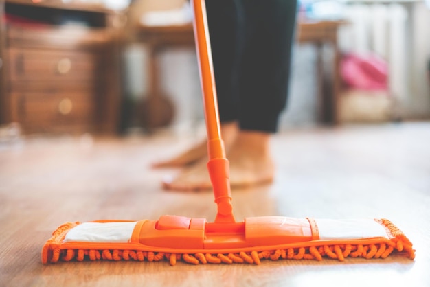 Hombre soltero sosteniendo un trapeador y limpiando el piso laminado en casa