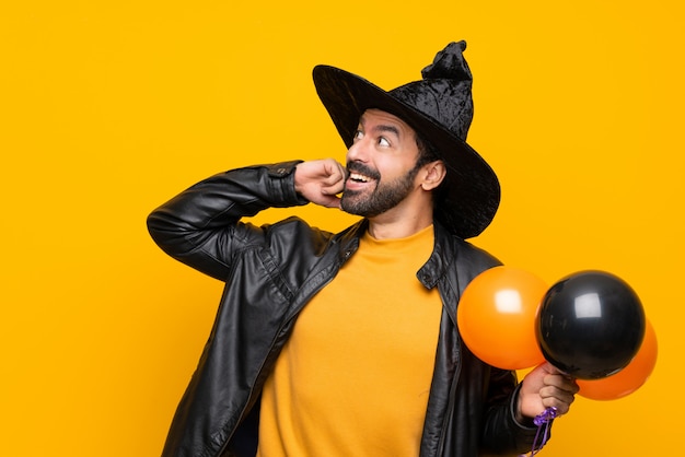 Hombre con sombrero de bruja sosteniendo globos negros y naranjas para la fiesta de halloween pensando en una idea