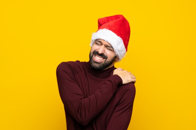 Hombre con sombrero de navidad con dolor en el hombro sobre fondo amarillo aislado