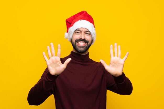 Hombre con sombrero de Navidad sobre pared amarilla aislada contando diez con los dedos