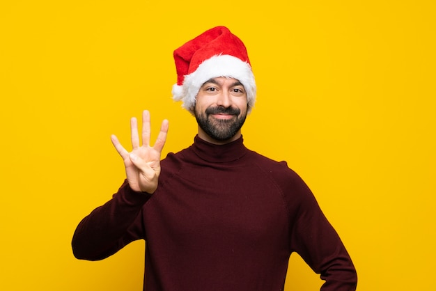 Hombre con sombrero de Navidad sobre pared amarilla aislada feliz y contando cuatro con los dedos