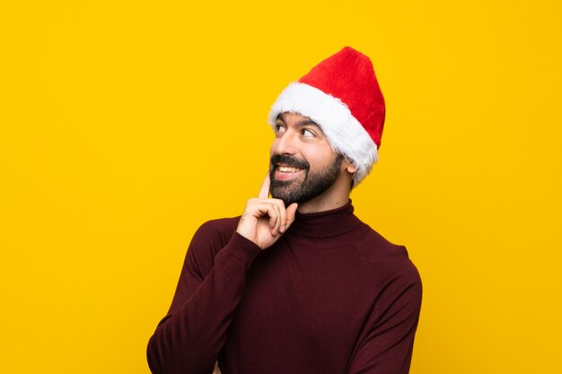 Hombre con sombrero de Navidad sobre pared amarilla aislada pensando una idea mientras mira hacia arriba