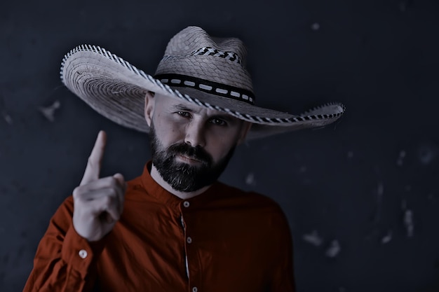 hombre con sombrero de paja con ala en el estudio hace gestos con las manos y los dedos, puntos. Estilo sambrero de américa occidental méxico