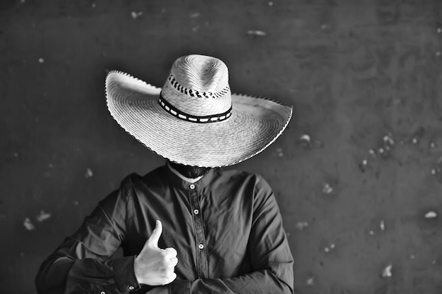 Foto hombre con sombrero de paja con ala en el estudio hace gestos con las manos y los dedos, puntos. estilo sambrero de américa occidental méxico