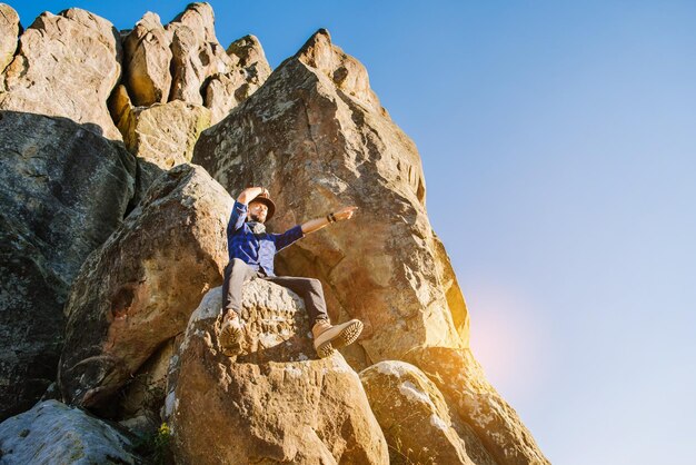 Un hombre con sombrero sentado en lo alto de las rocas en el fondo del cielo azul