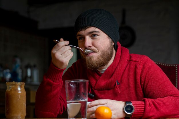 Un hombre con sombrero y suéter desayuna en la cocina.