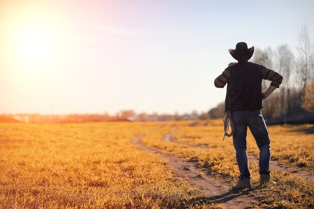 Un hombre con sombrero de vaquero y un loso en el campo. Granjero estadounidense en un campo con un sombrero de jeans y con un loso. Un hombre camina por el campo con sombrero