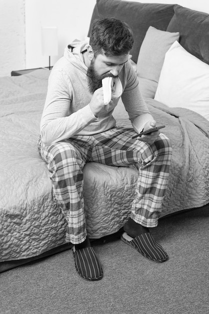 Hombre somnoliento brutal desayuna en el dormitorio hombre maduro con barba en pijama en la cama dormir y despierto estilo de vida saludable hombre barbudo hipster comer plátano en la mañana Charlando con novia