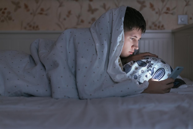 Hombre somnoliento con teléfono en la mano y navegando por la web antes de dormir adicción a las redes sociales trastorno del sueño