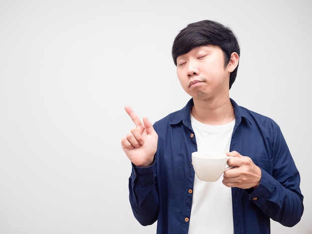 Hombre soñoliento sosteniendo la taza de café cerrar los ojos y señalar con el dedo en el espacio de la copia fondo blanco.