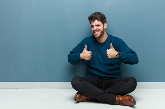 hombre sonriendo ampliamente mirando feliz, positivo, seguro y exitoso, con ambos pulgares arriba