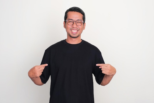 Un hombre sonriendo a la cámara mientras señala la camiseta negra que lleva puesta