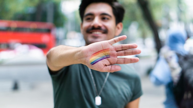 Hombre sonriendo y cubriendo la cámara con la mano con maquillaje de arco iris.