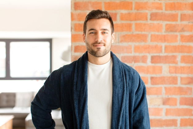 Hombre sonriendo felizmente con una mano en la cadera y actitud confiada, positiva, orgullosa y amistosa