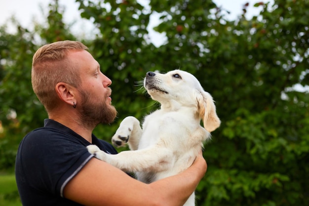 Hombre sonriendo mientras sostiene un juguetón cachorro de golden retriever al aire libre en verano