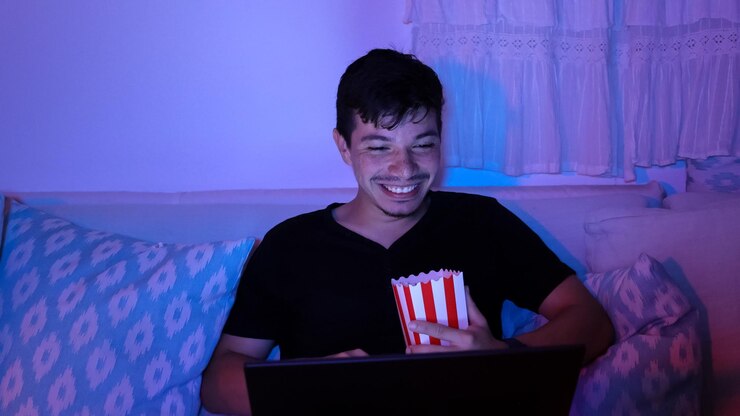 Hombre sonriendo mientras ve una película en su computadora