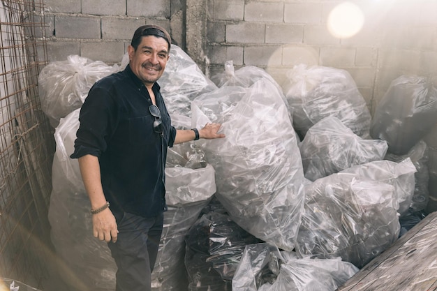 Hombre sonriendo y mirando a la cámara mostrando sus bolsas de trabajo de reciclaje llenas de botellas de plástico